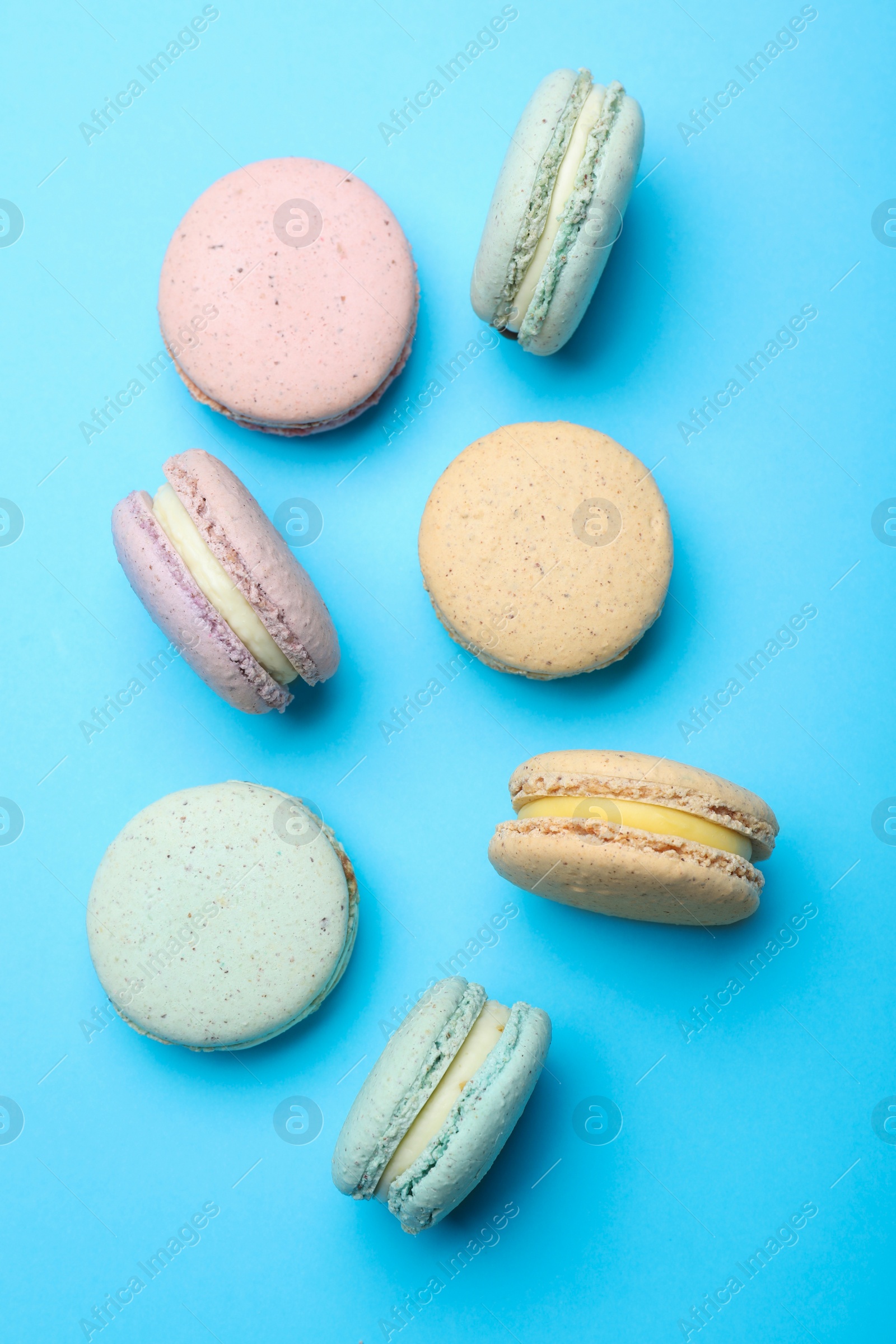 Photo of Delicious colorful macarons on light blue background, flat lay