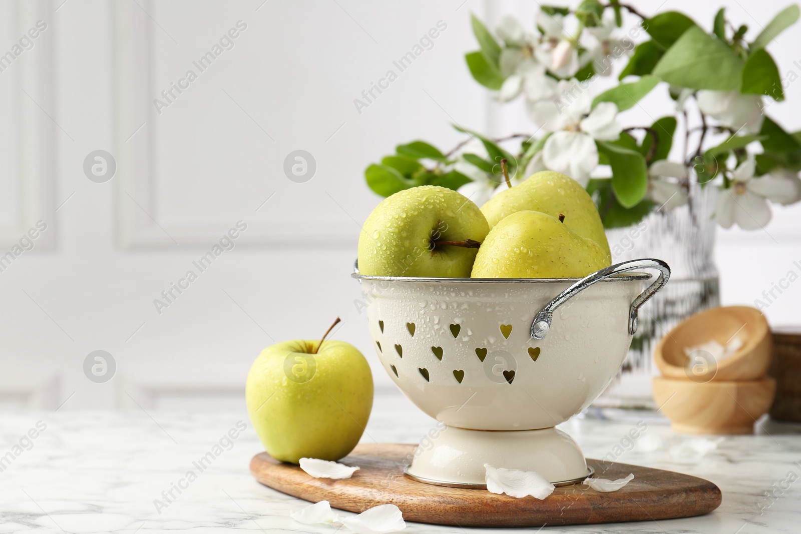 Photo of Colander with fresh apples and flower petals on white marble table, space for text