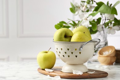 Photo of Colander with fresh apples and flower petals on white marble table, space for text