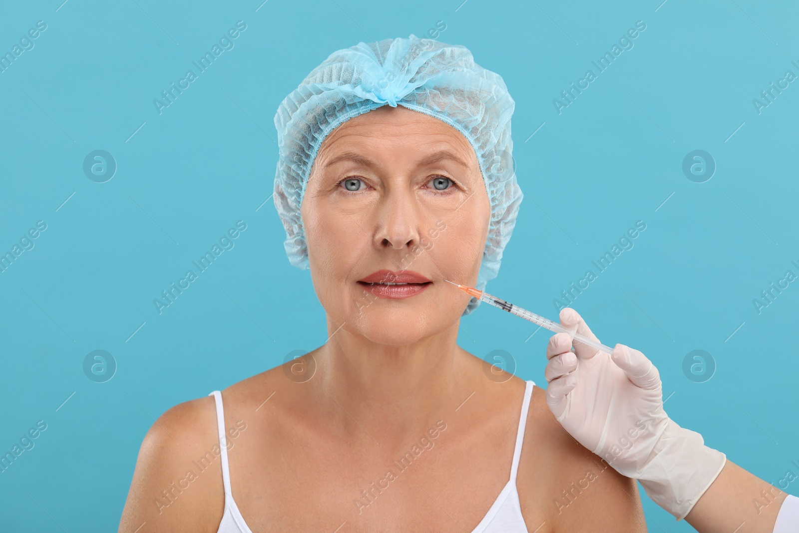 Photo of Doctor giving facial injection to senior woman on light blue background. Cosmetic surgery