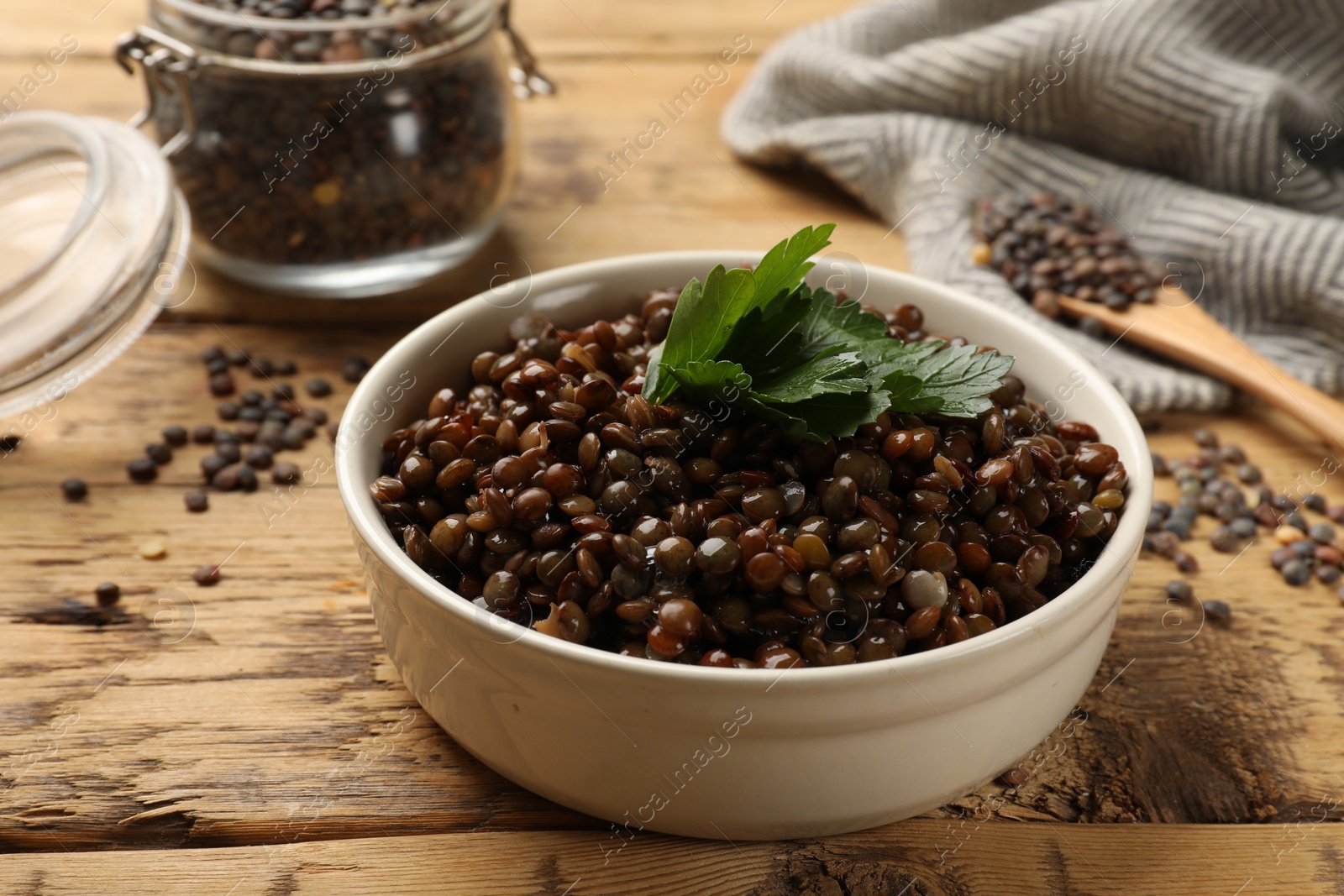 Photo of Delicious lentils with parsley in bowl on wooden table, closeup