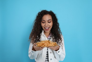 Photo of Excited African American woman with French fries on light blue background