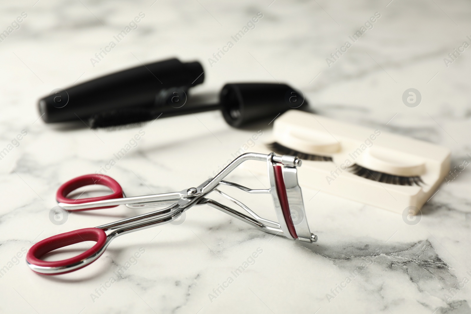 Photo of False eyelashes, curler and mascara on white marble table, closeup