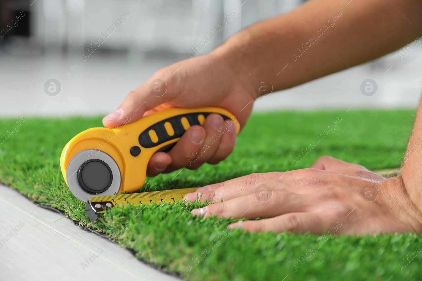 Photo of Man cutting artificial grass carpet indoors, closeup