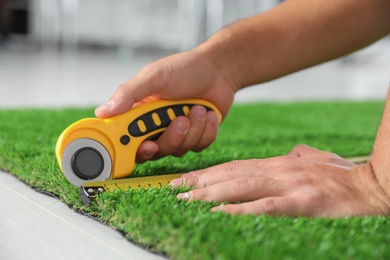 Photo of Man cutting artificial grass carpet indoors, closeup