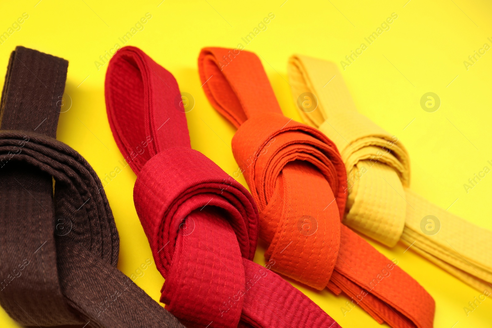 Photo of Colorful karate belts on yellow background, closeup