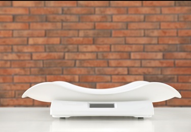 Photo of Modern digital baby scales on table against brick wall. Space for text