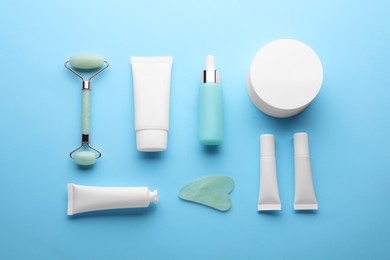 Photo of Natural face roller, gua sha tool and cosmetic products on light blue background, flat lay