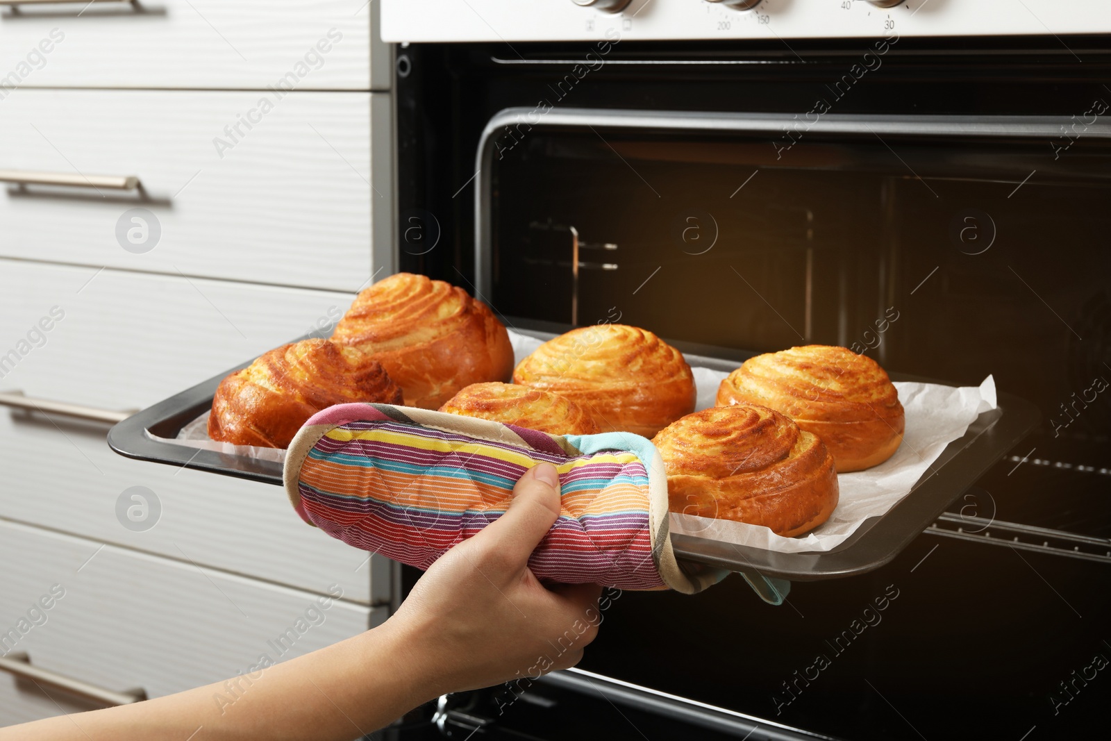 Photo of Woman taking freshly baked buns out of oven, closeup