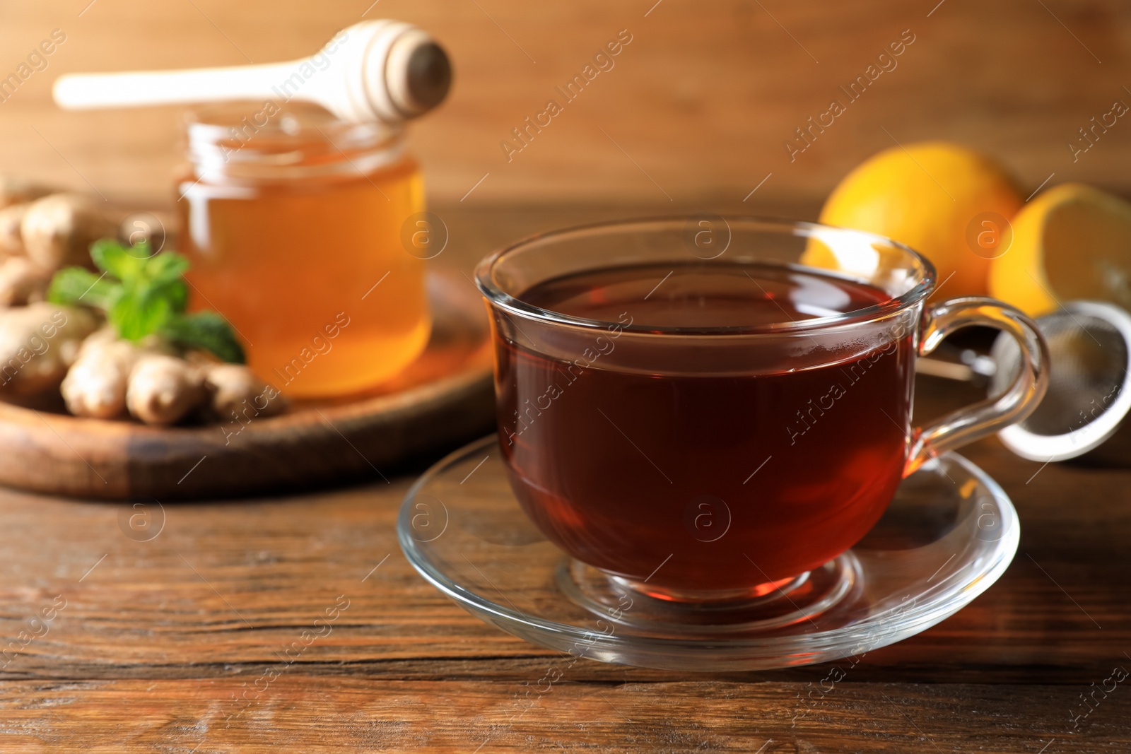 Photo of Cup of delicious ginger tea and ingredients on wooden table, closeup