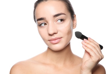 Photo of Young woman applying foundation on her face against white background