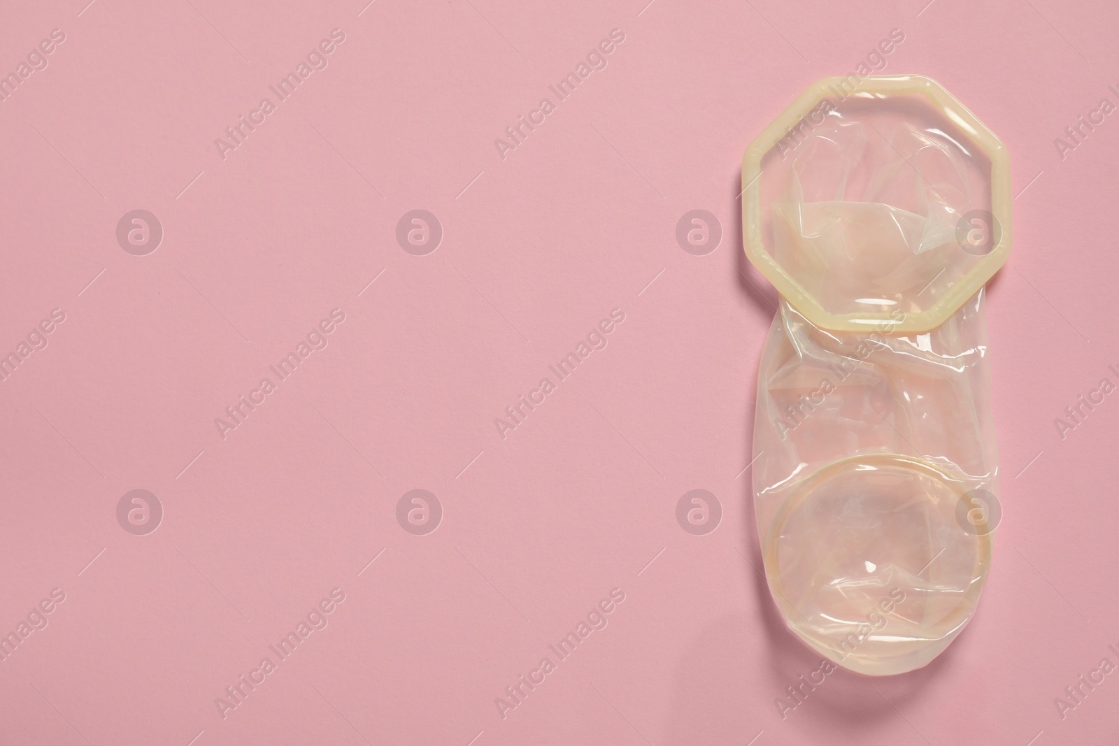 Photo of Unrolled female condom on light pink background, top view and space for text. Safe sex
