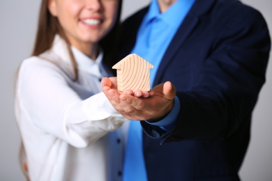 Young couple holding house figure on grey background, closeup. Home insurance