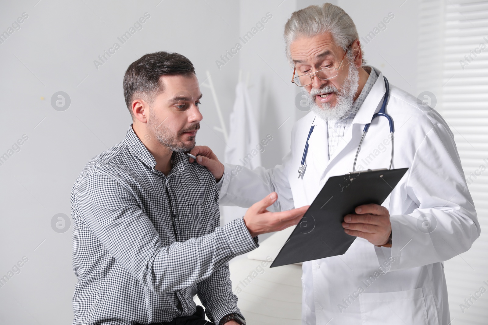 Photo of Senior doctor with clipboard consulting patient in clinic