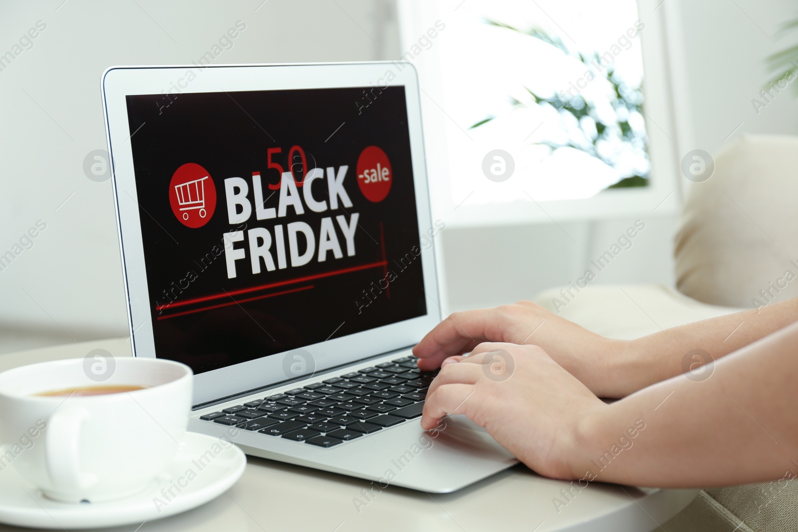 Photo of Woman using laptop with Black Friday announcement on screen at table, closeup