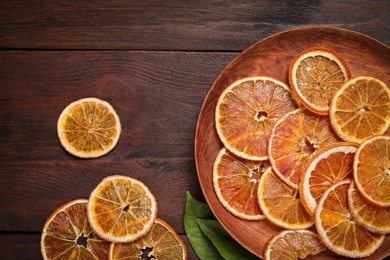 Photo of Delicious dried orange slices and green leaves on wooden table, flat lay