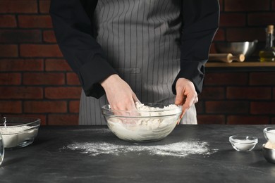 Photo of Making bread. Woman preparing dough in bowl at grey textured table in kitchen, closeup