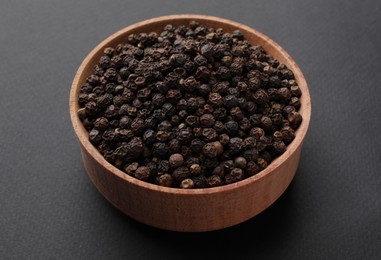 Photo of Wooden bowl of black peppercorns on dark background