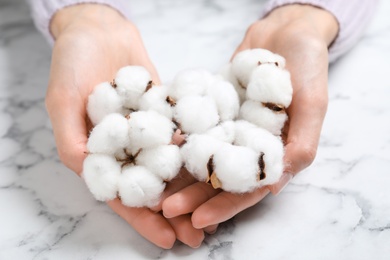 Photo of Young woman with fluffy cotton flowers at marble table, closeup