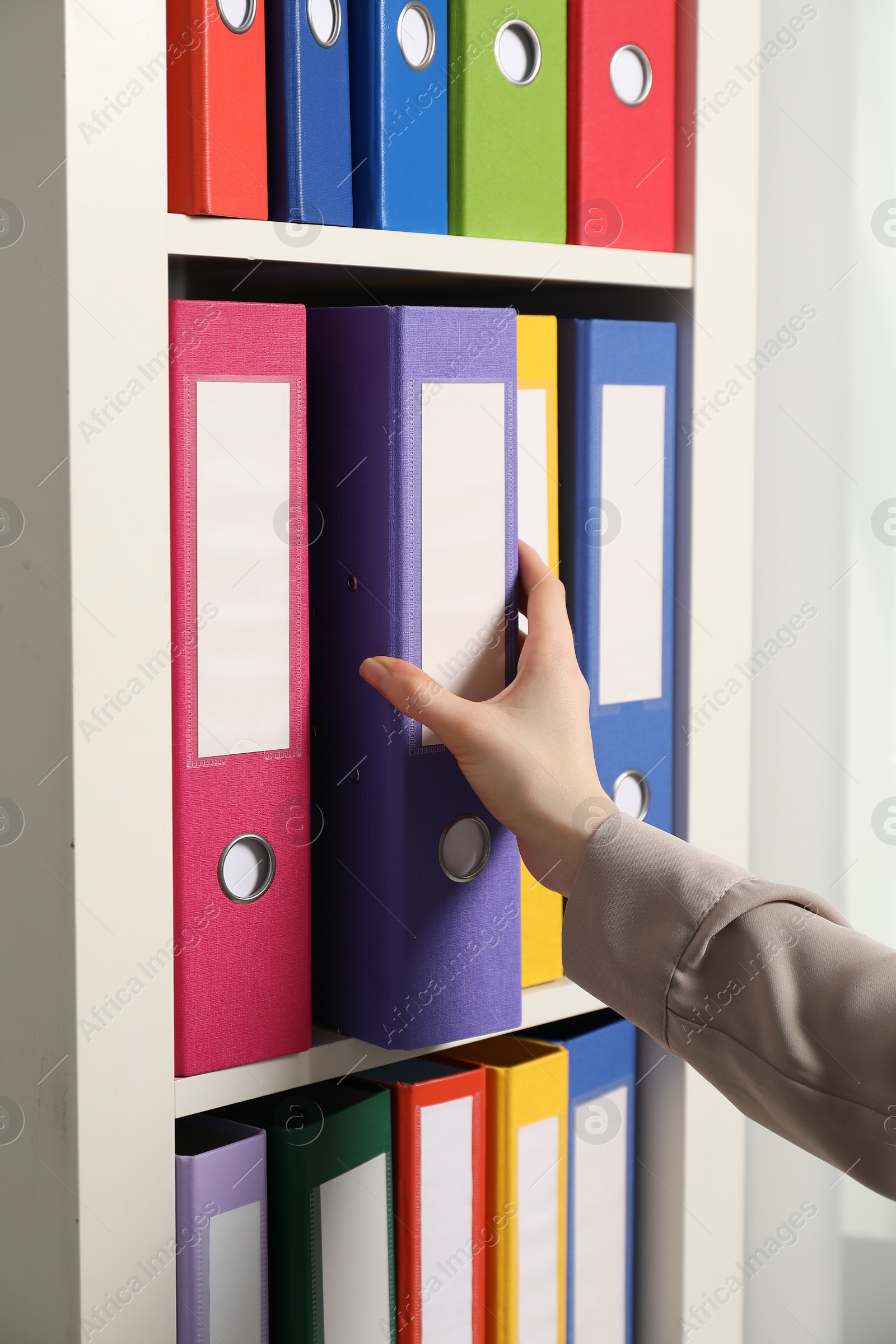 Photo of Woman taking binder office folder from shelving unit indoors, closeup