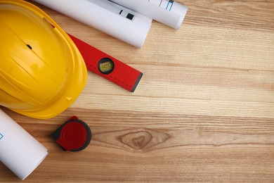 Construction drawings, safety hat, tape measure and bubble level on wooden table, flat lay. Space for text