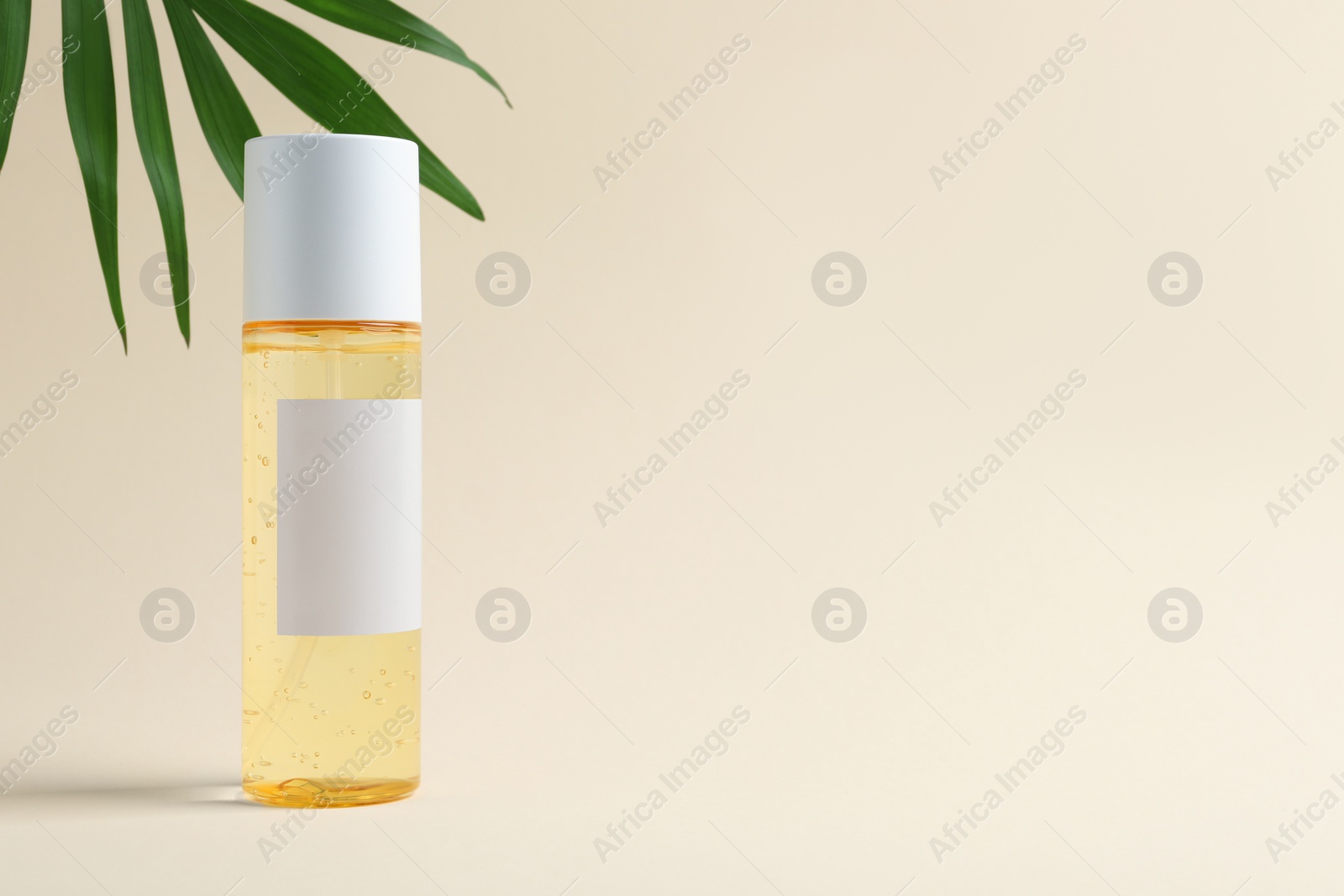 Photo of Bottle with cosmetic oil and green leaf on beige background. Space for text
