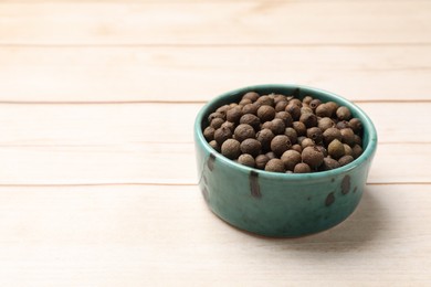 Photo of Dry allspice berries (Jamaica pepper) in bowl on light wooden table, space for text