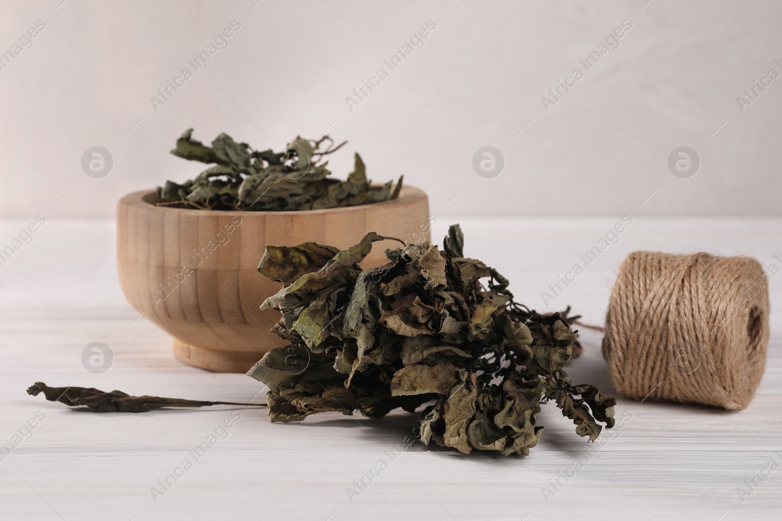 Photo of Bowl with dry basil and spool of twine on white wooden table