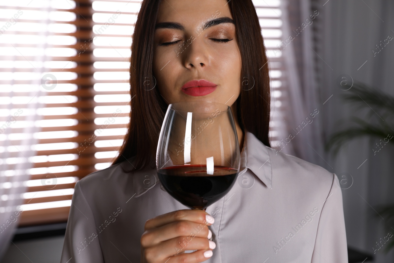 Photo of Beautiful young woman with glass of luxury red wine indoors