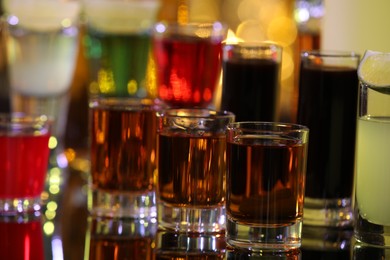 Photo of Different shooters in shot glasses on mirror surface against blurred background, closeup. Alcohol drink