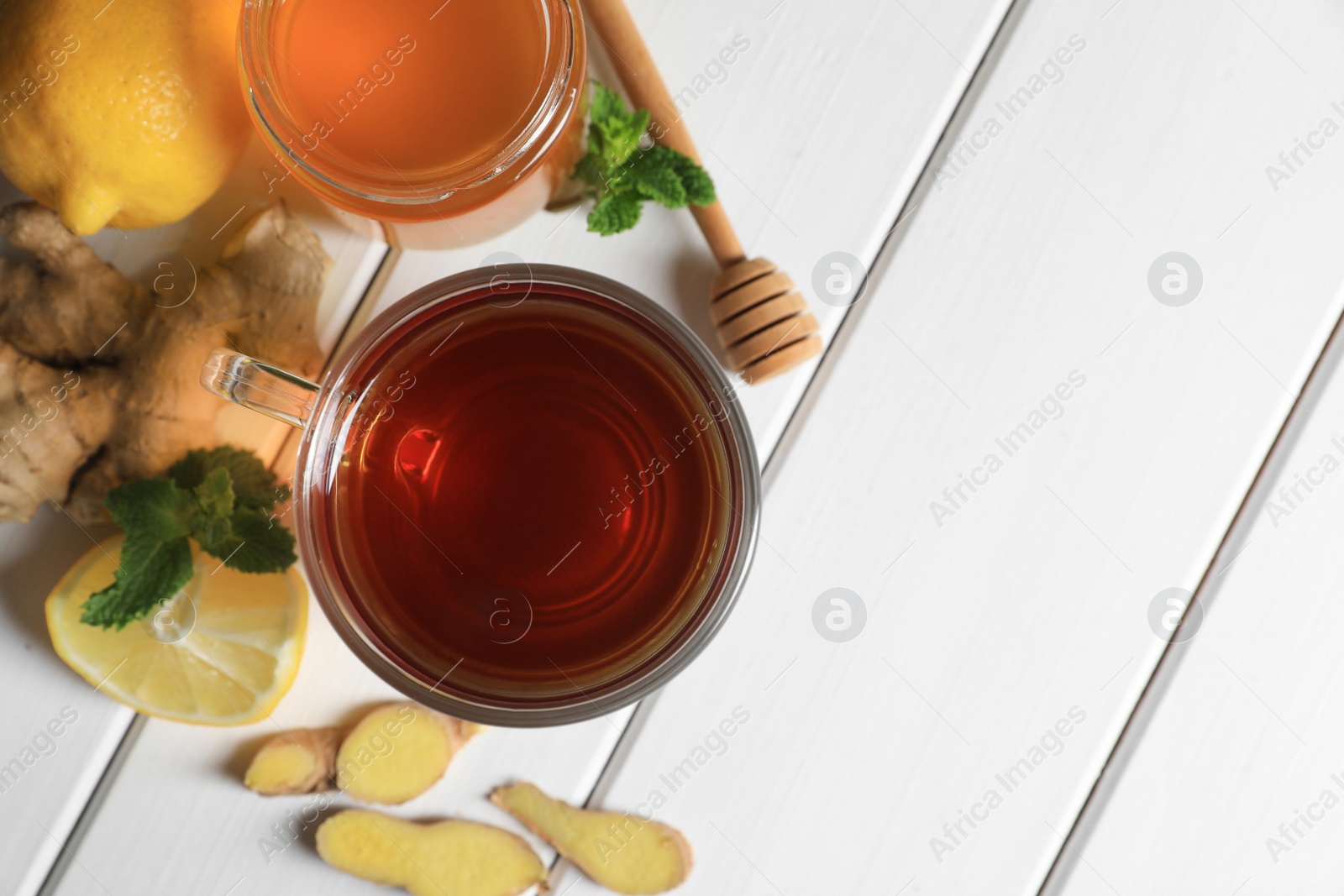 Photo of Cup of delicious ginger tea, honey and lemons on white wooden table, flat lay. Space for text