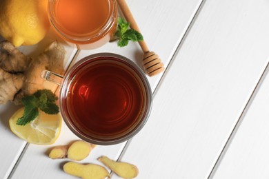 Photo of Cup of delicious ginger tea, honey and lemons on white wooden table, flat lay. Space for text