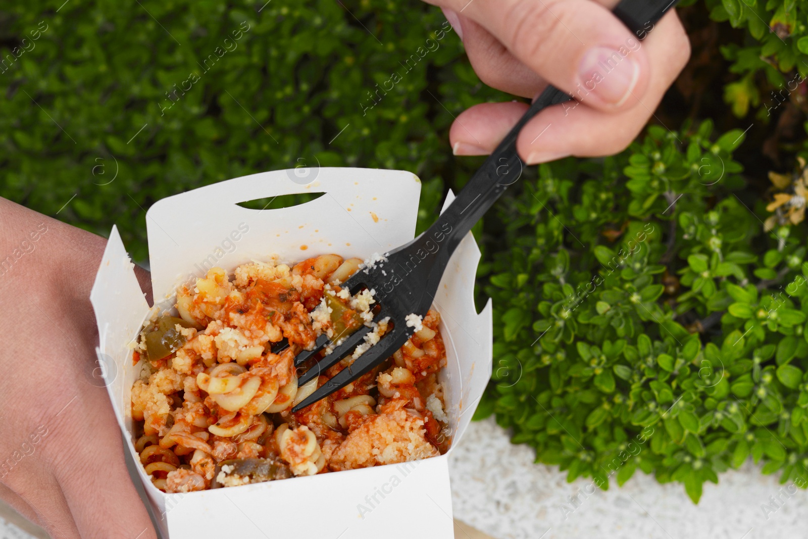 Photo of Woman eating takeaway noodles from paper box with fork outdoors, closeup. Street food