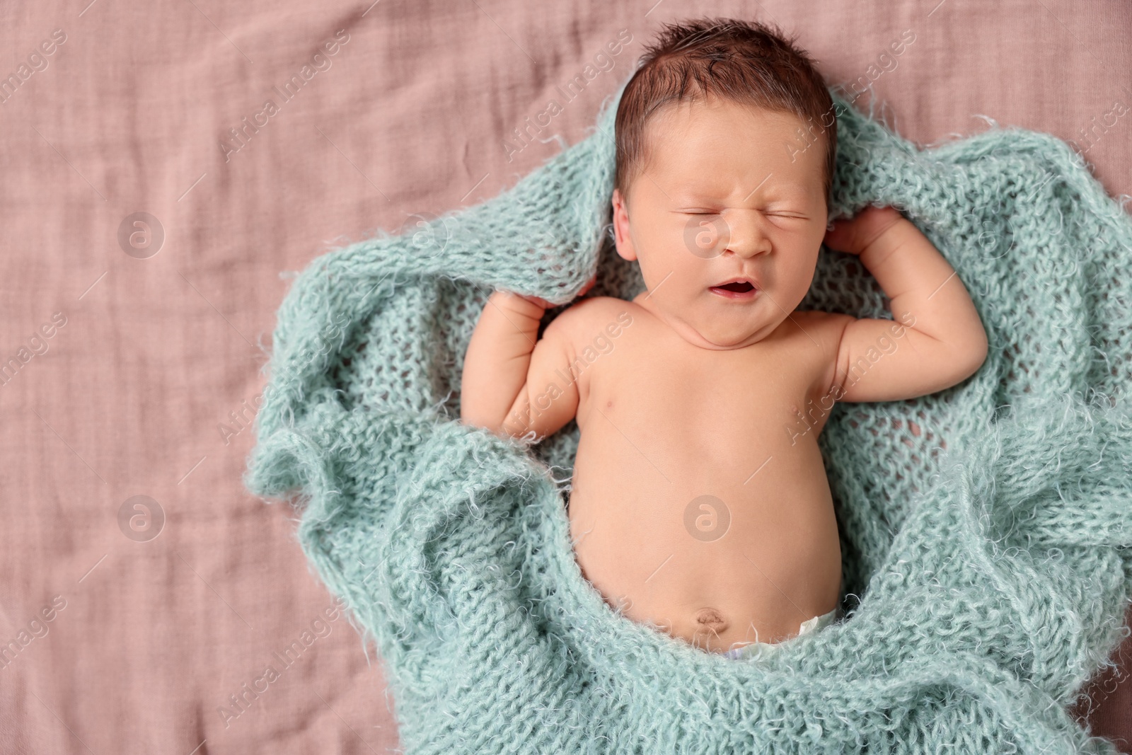 Photo of Cute newborn baby in turquoise knitted blanket yawning on bed, top view. Space for text