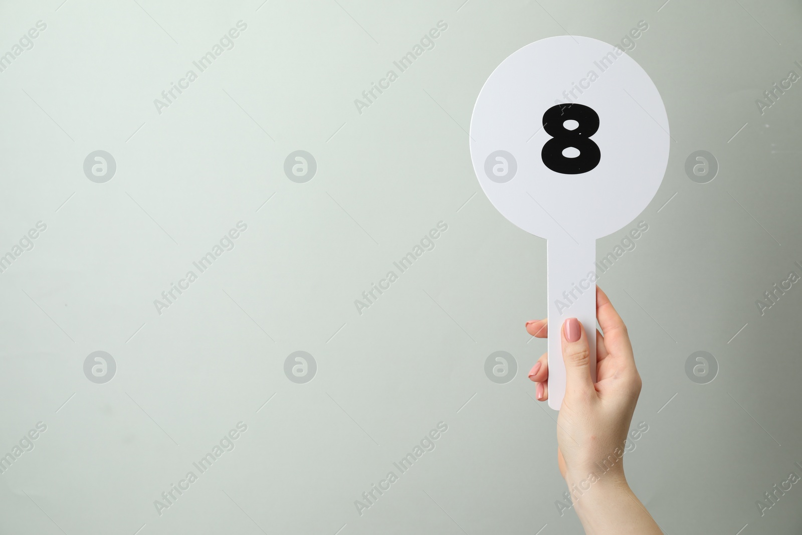 Photo of Woman holding auction paddle with number 8 on light grey background, closeup. Space for text