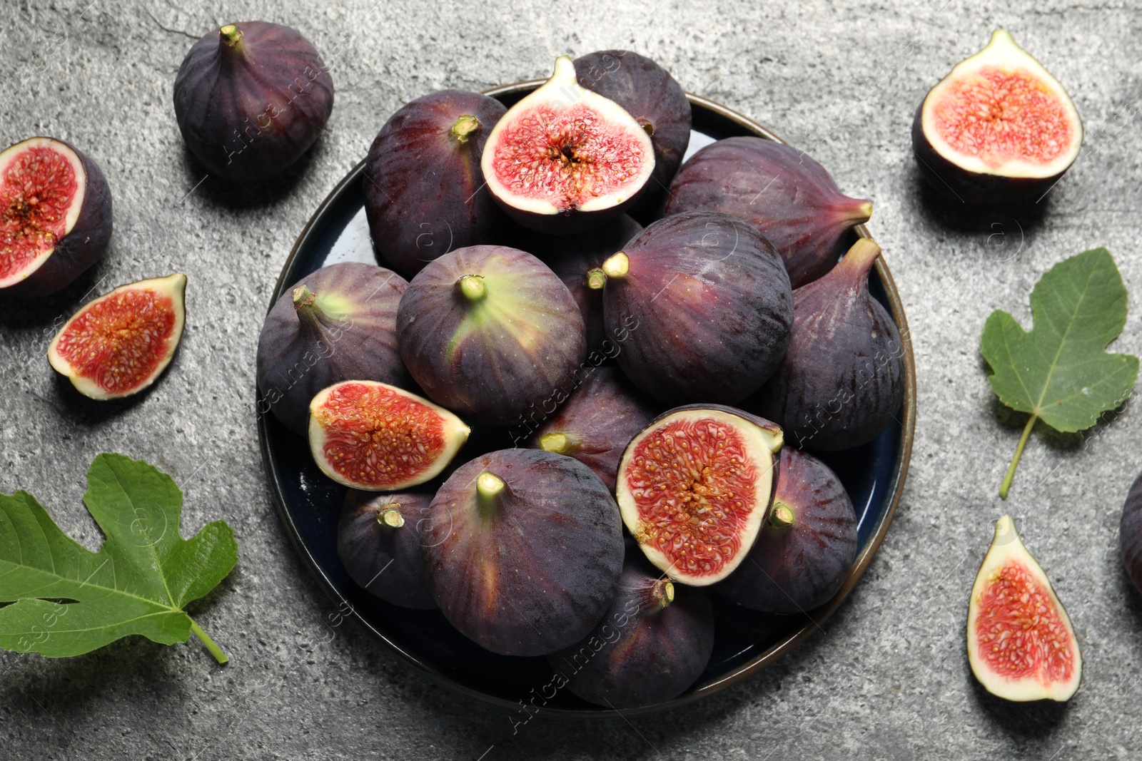 Photo of Whole and cut ripe figs with leaves on light grey textured table, flat lay