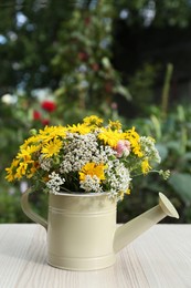 Beautiful bouquet of bright wildflowers in watering can on white wooden table outdoors