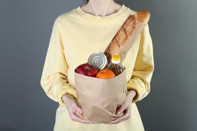 Humanitarian aid. Woman with food products for donation on grey background, closeup