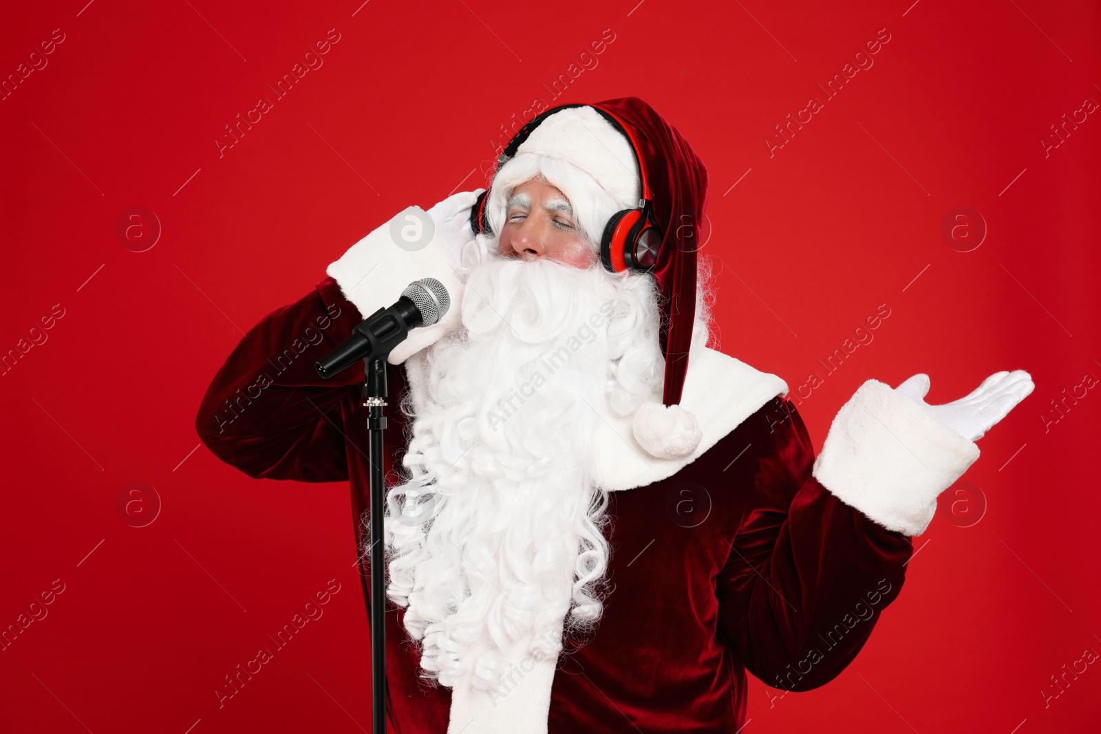 Photo of Santa Claus with headphones and microphone on red background. Christmas music
