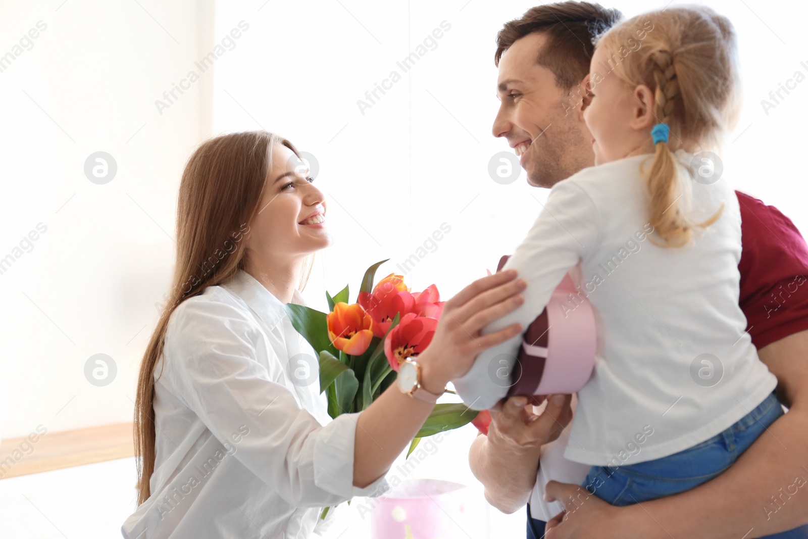 Photo of Happy woman receiving flowers and gift from her family at home. Mother's day celebration