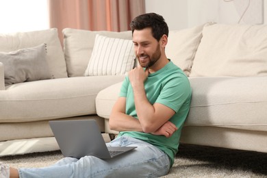 Photo of Man using laptop on floor near sofa at home