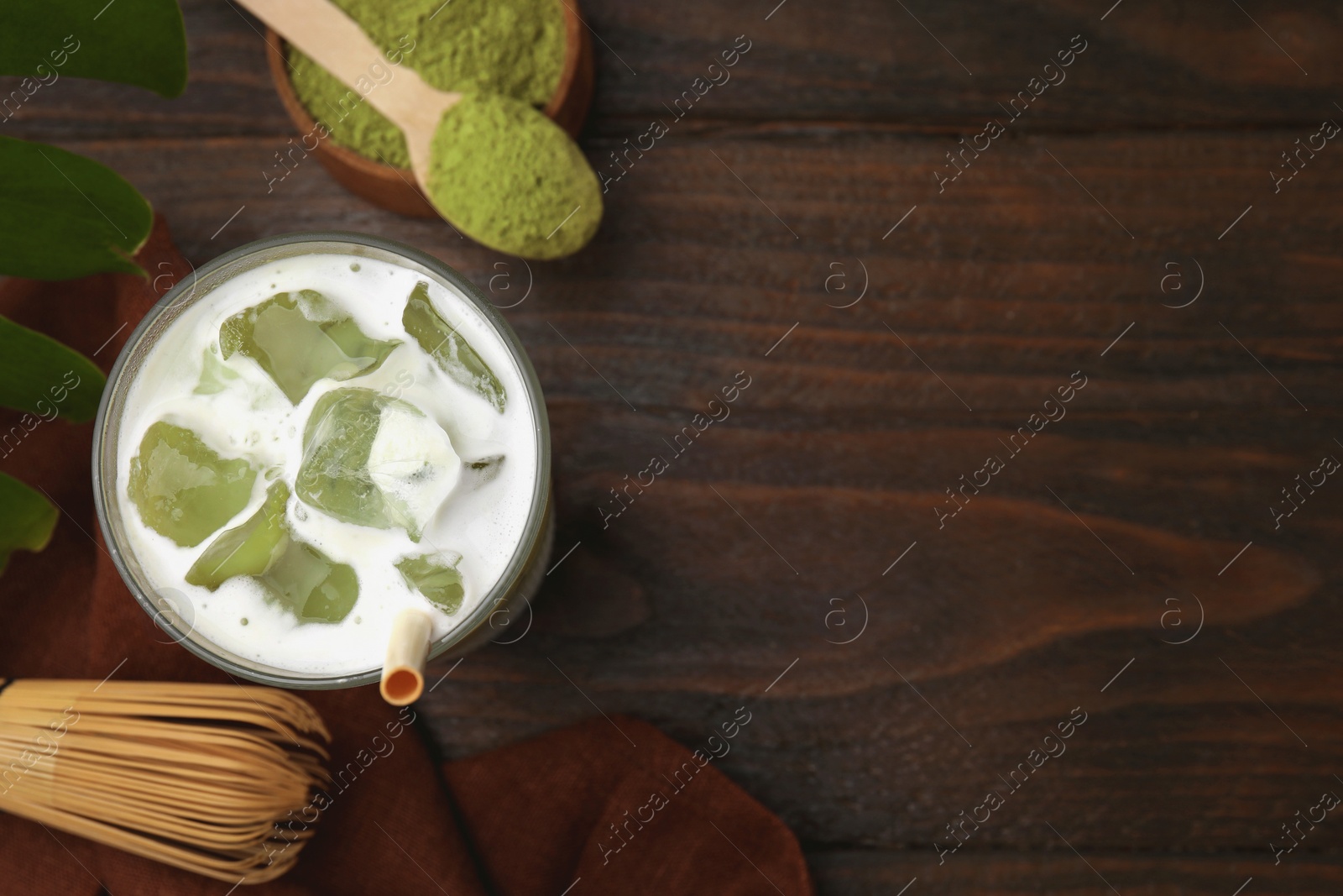 Photo of Glass of tasty iced matcha latte, bamboo whisk and powder on wooden table, flat lay. Space for text