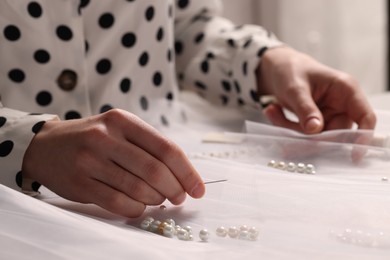 Photo of Dressmaker with sewing accessories at white table in atelier, closeup