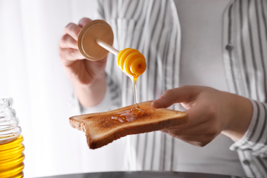 Woman pouring honey onto toasted bread, closeup