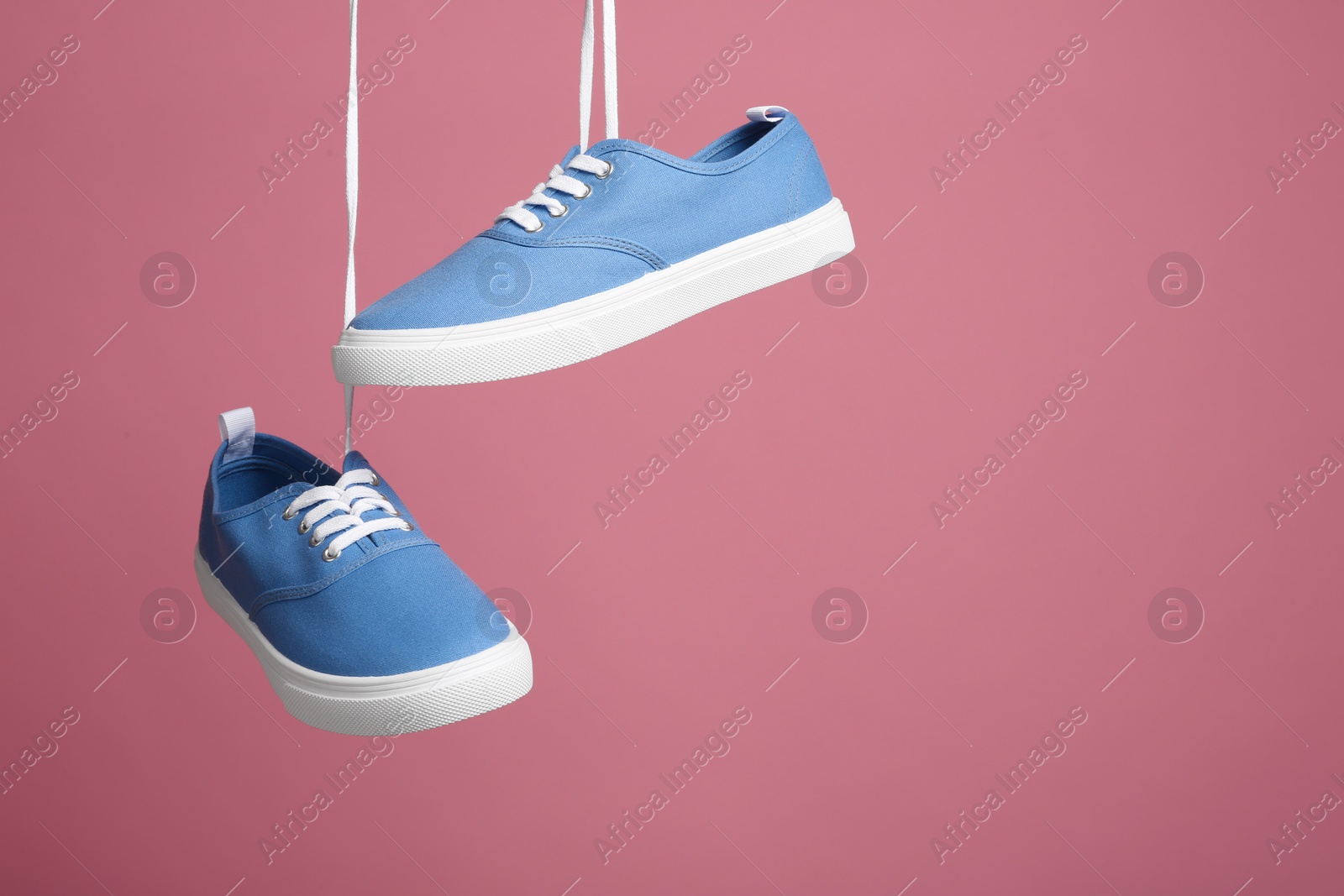 Photo of Pair of bright stylish shoes hanging against color background. Space for text