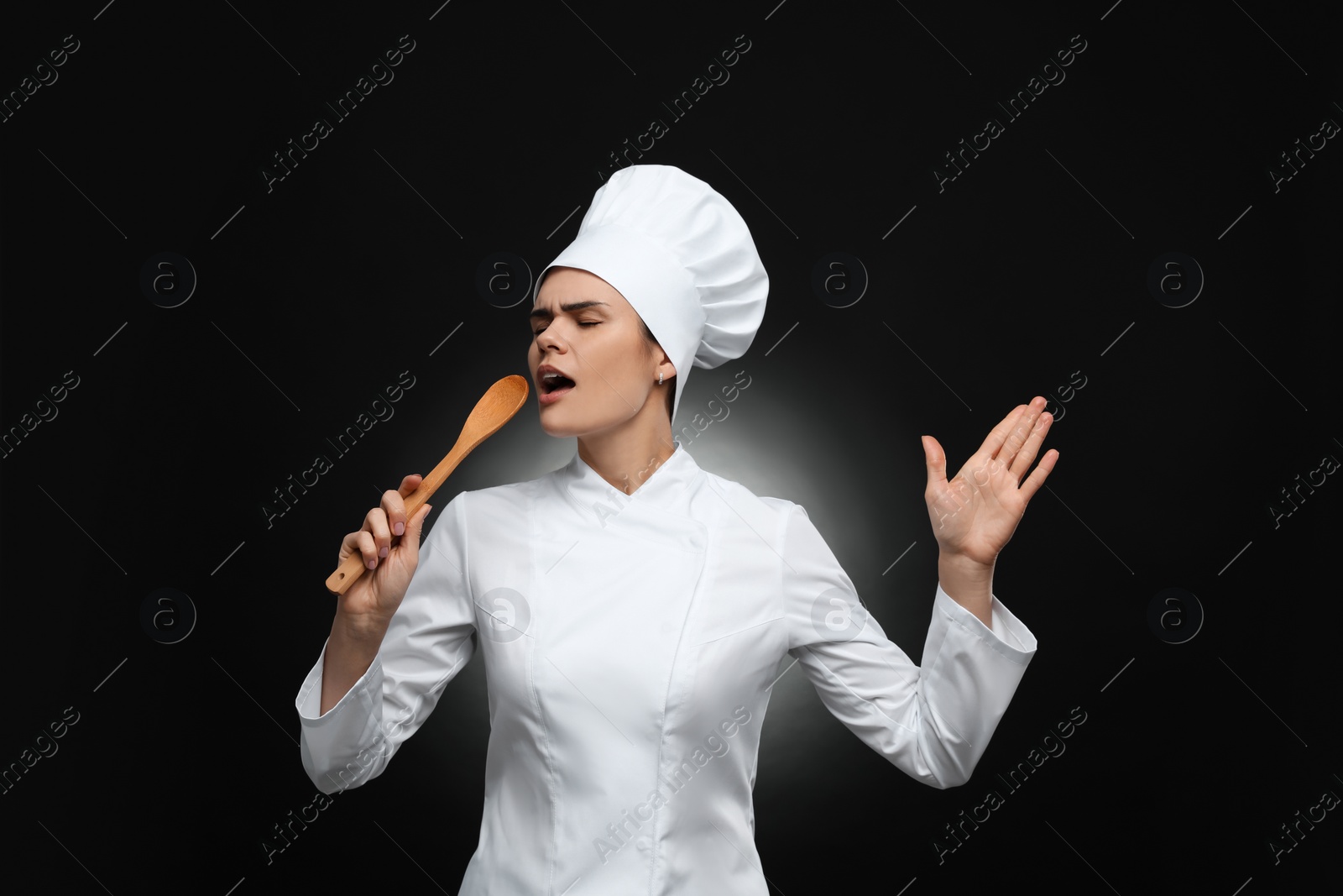 Photo of Emotional female chef singing with wooden spoon on black background