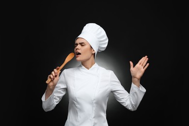 Emotional female chef singing with wooden spoon on black background