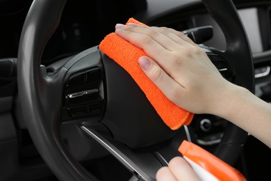 Photo of Woman cleaning steering wheel with rag in car, closeup