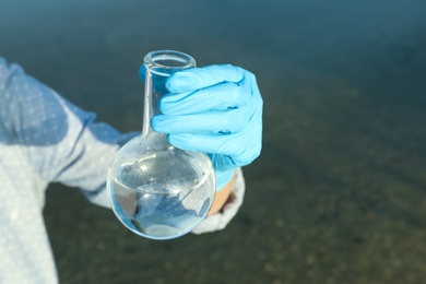 Photo of Scientist with florence flask taking sample from river for analysis, closeup