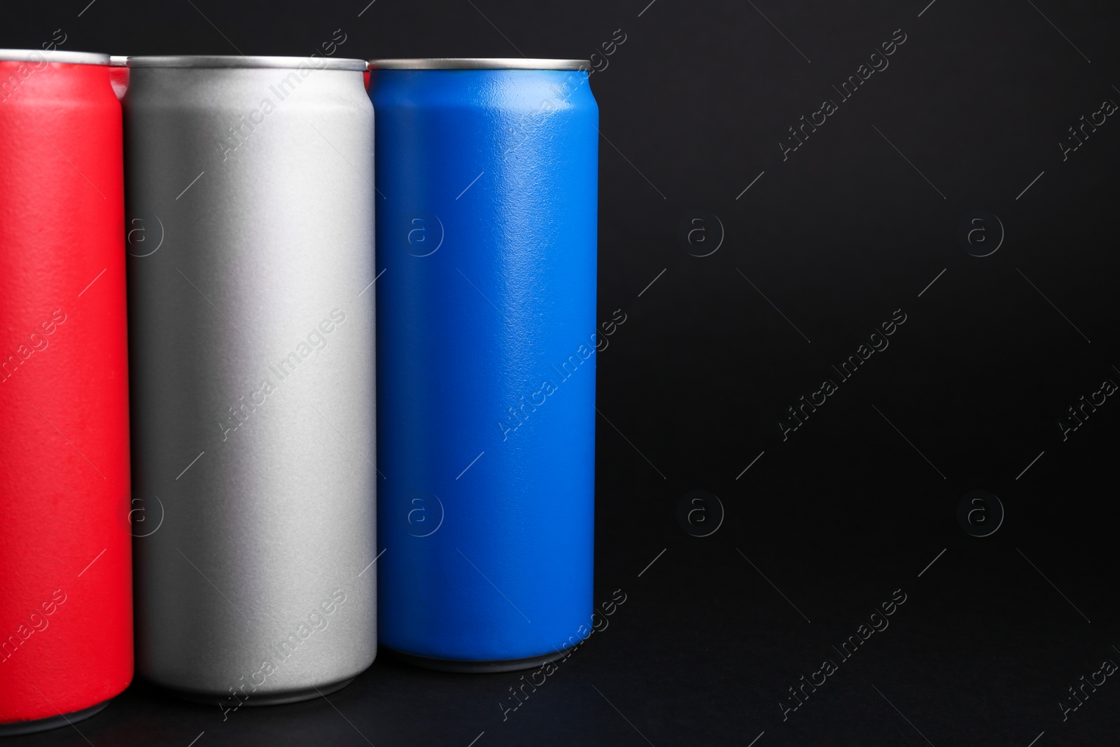 Photo of Energy drinks in colorful cans on black background, space for text